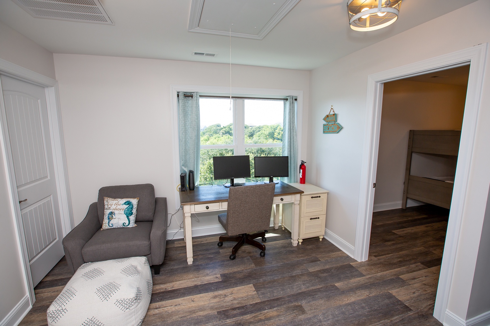 Your private workspace awaits with dual monitors, comfortable seating, and inspiring tree views through the window.