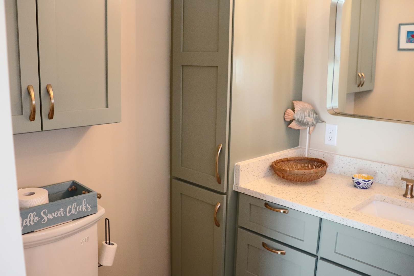 Your stylish kitchen features sage-green cabinets, gold hardware, and quartz countertops—perfect for preparing meals with coastal charm and modern elegance.