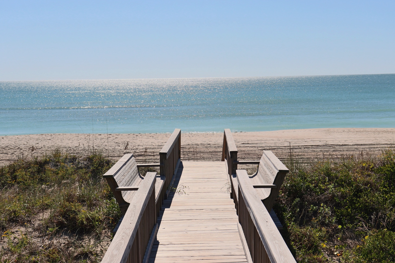 Wooden walkway leads directly to pristine beach with turquoise waters and soft sand stretching endlessly along the coastline.