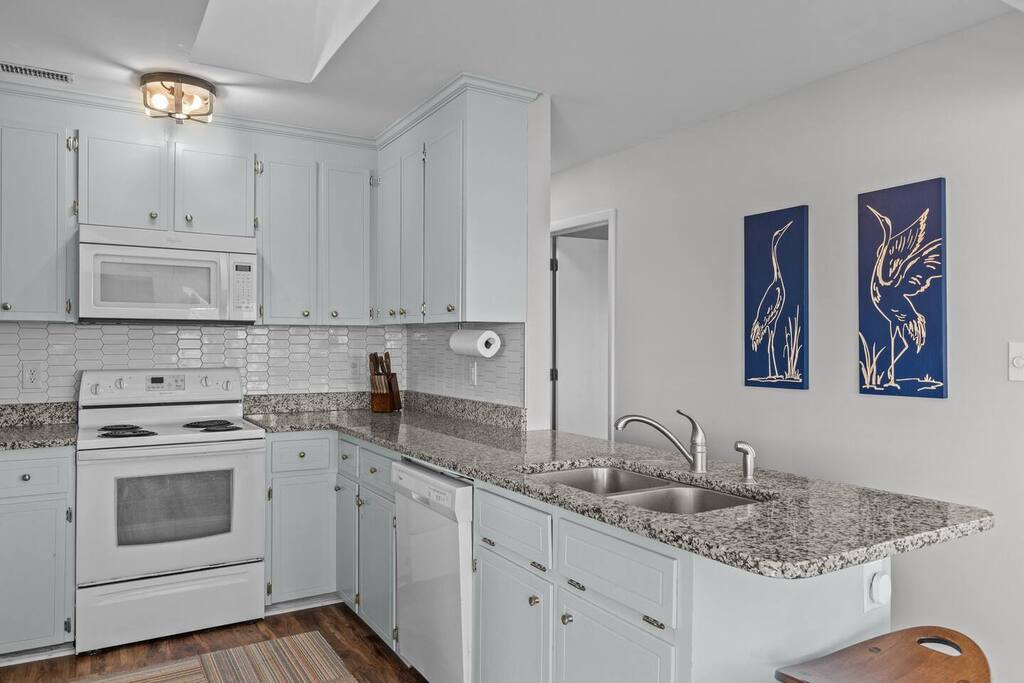 Your fully equipped kitchen features granite countertops, white appliances, and cheerful artwork - perfect for preparing meals during your stay.