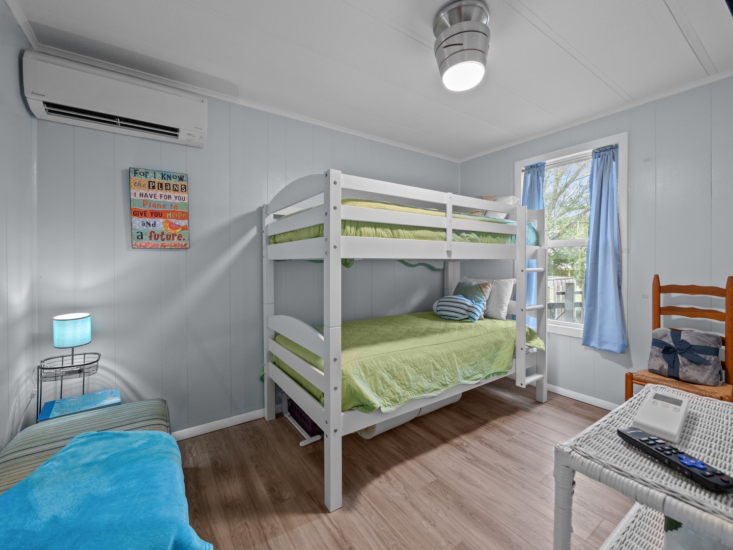 This comfortable bedroom features bunk beds perfect for kids, with fresh green linens and a cozy blue reading chair by the window.