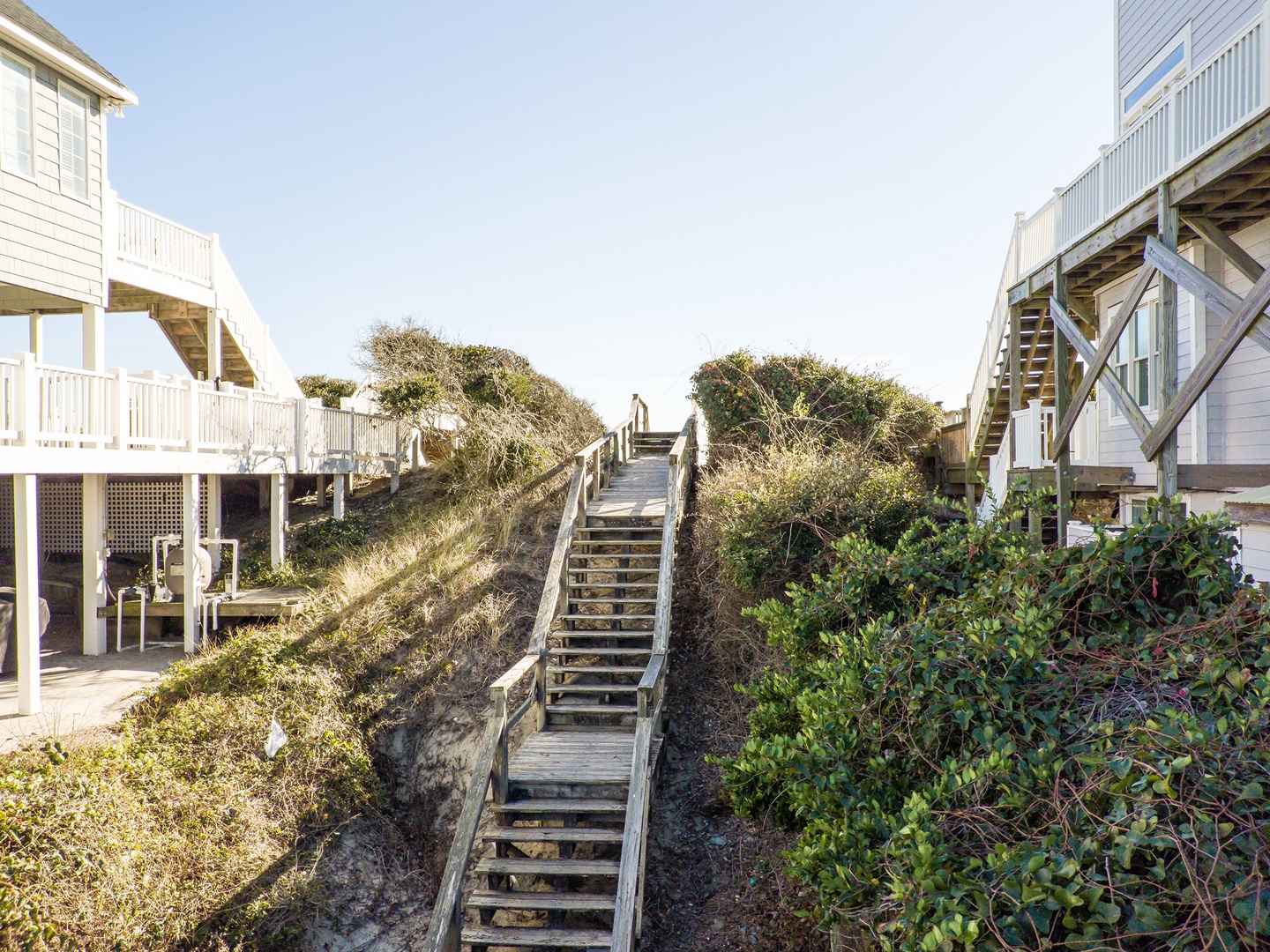 Beach access stairway winds through coastal dunes, connecting charming waterfront cottages to the shoreline below.