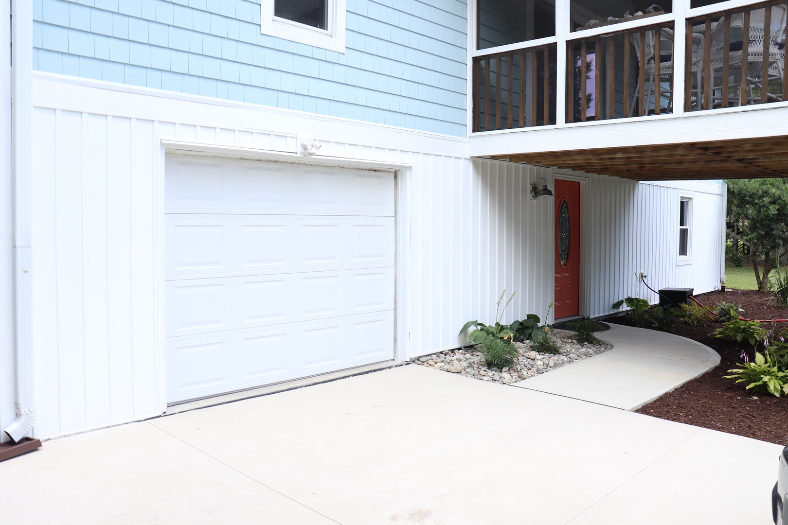 Modern beachside property featuring convenient garage parking and welcoming red front door entrance with covered walkway.