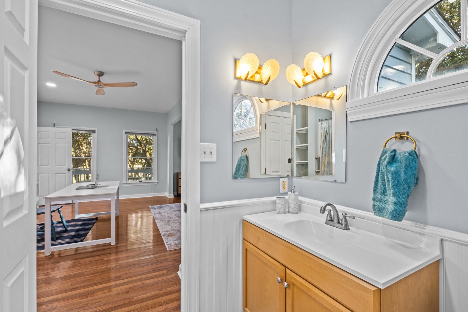 Step into your bright bathroom featuring warm wood vanity, elegant lighting, and thoughtful touches like the soft teal towel.