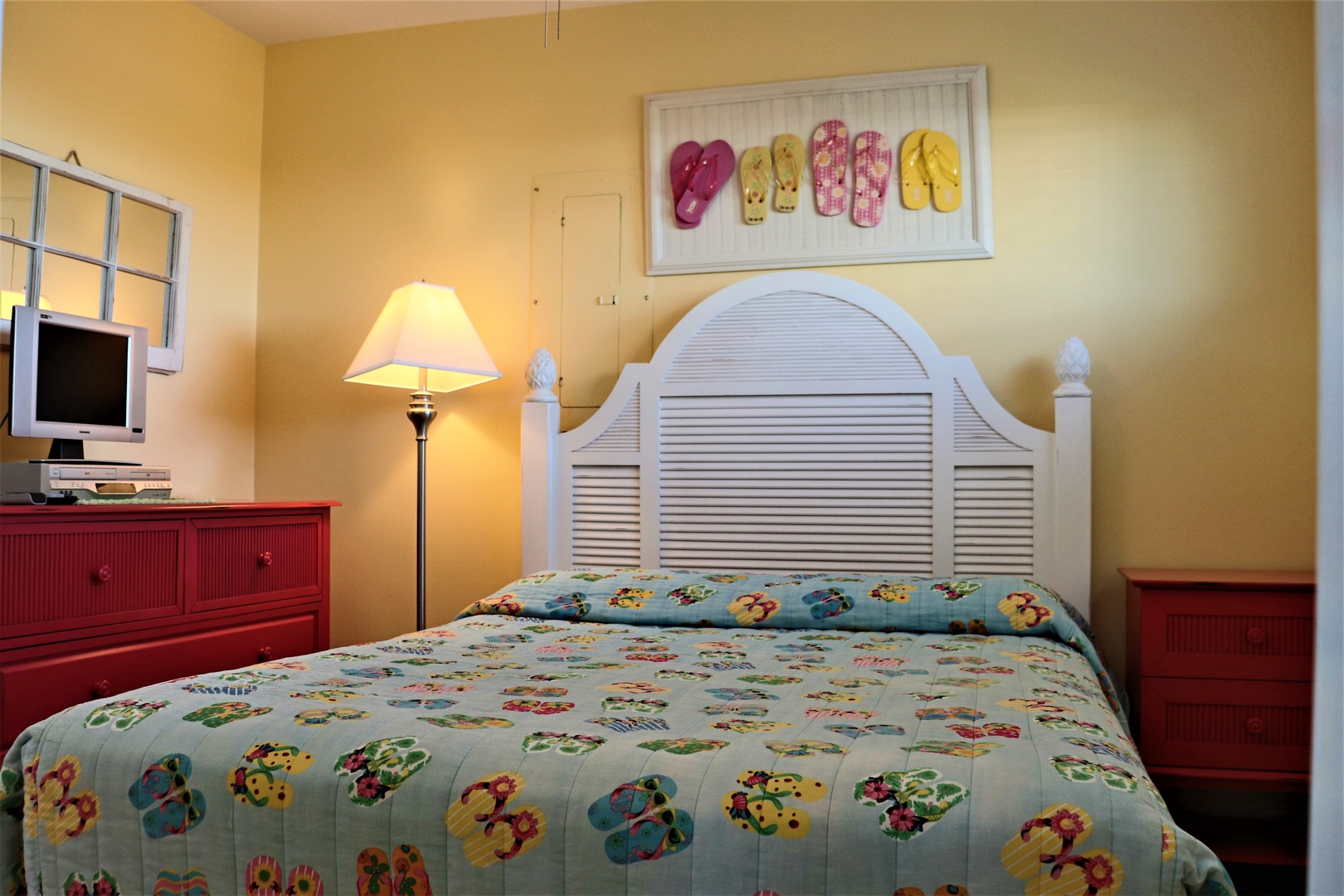 Your cheerful bedroom features a comfortable bed with tropical-themed linens and coastal flip-flop art that sets the perfect vacation mood.