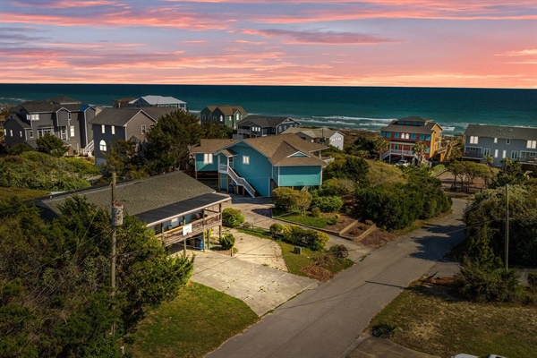 Coastal vacation rental community captured during golden hour with colorful beachfront homes nestled among lush greenery near the ocean.