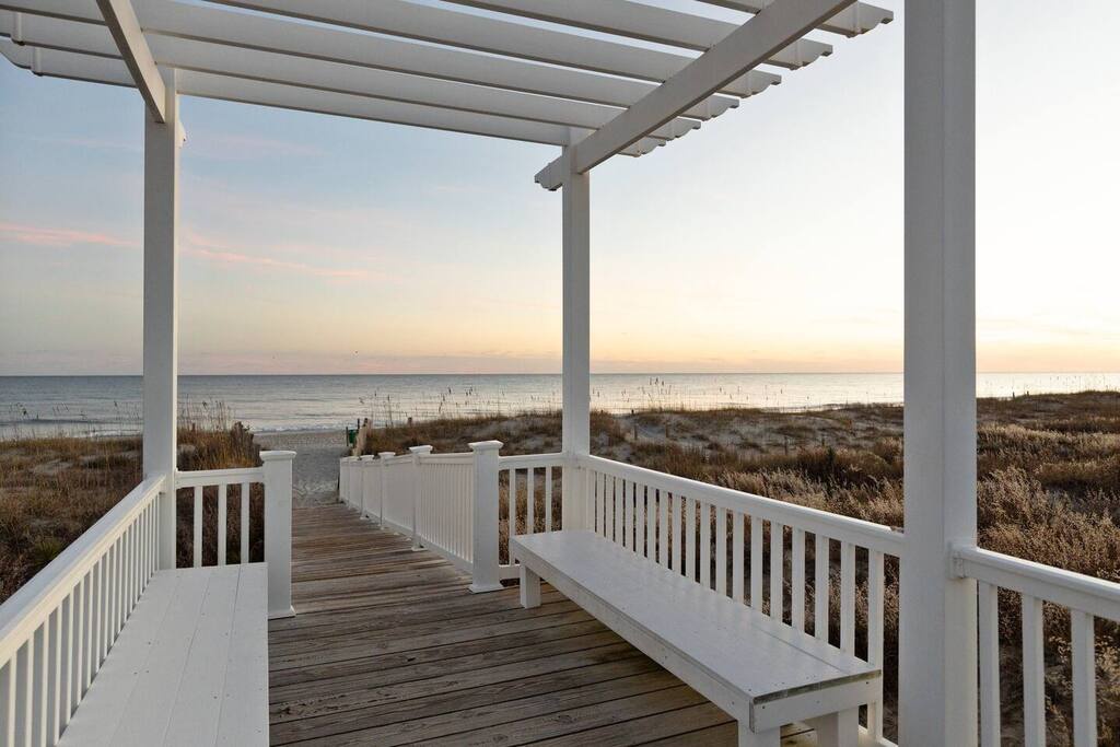 This covered deck overlooks pristine sandy beaches and coastal dunes, offering an elevated view of the shoreline at golden hour.