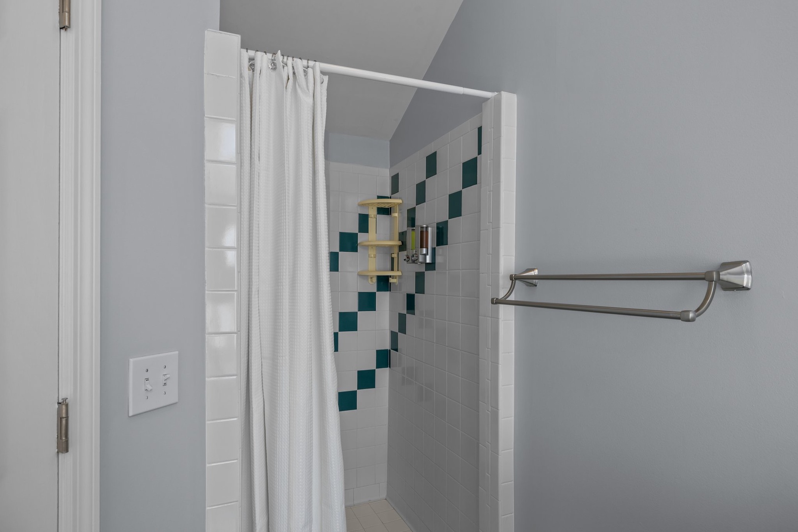 Step into your private bathroom featuring a spacious walk-in shower with beautiful teal accent tiles and convenient grab bars for safety.