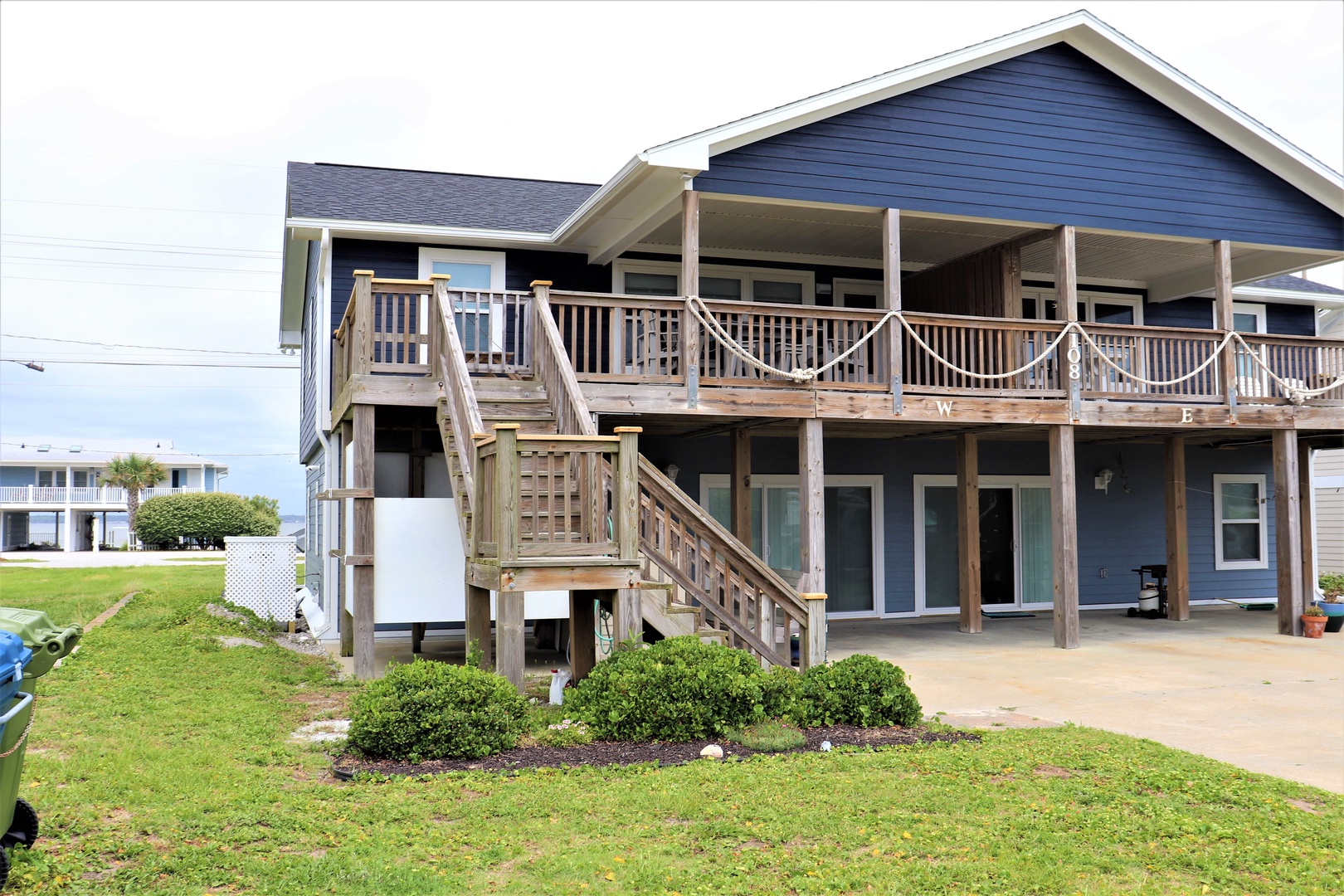 Charming coastal home with spacious covered deck and stairs leading to elevated entrance, surrounded by well-maintained landscaping.