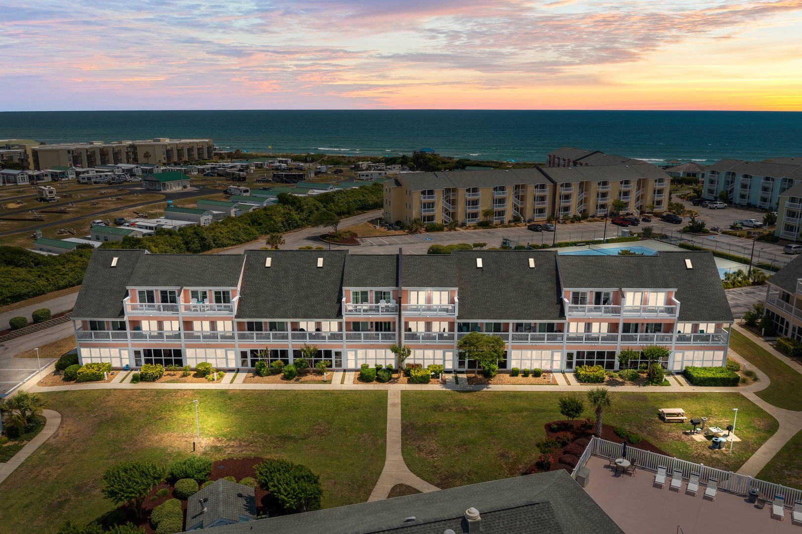 Coastal property complex featuring oceanfront accommodations with dramatic sunset skies over the Atlantic, surrounded by well-maintained grounds and nearby beach access.