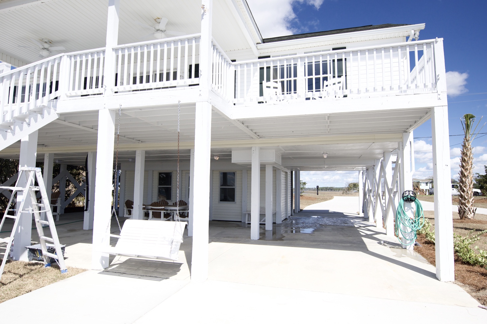 Elevated beach house featuring covered parking and wraparound balconies with white railings under sunny skies.