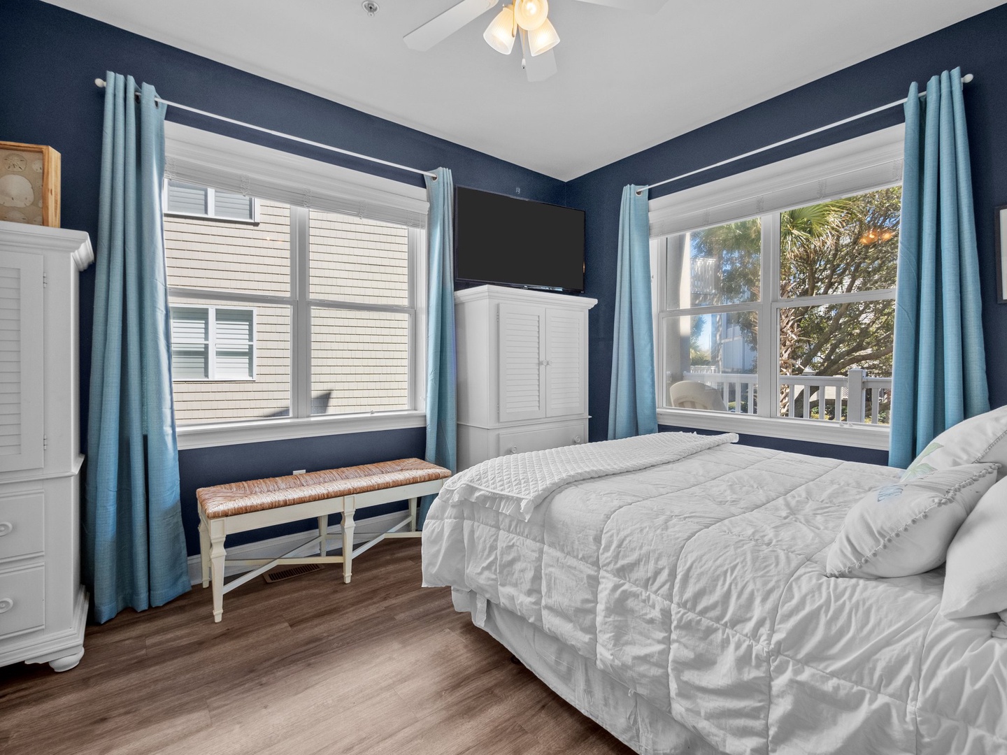 Your peaceful bedroom retreat features calming blue walls and crisp white linens, with windows offering natural light and coastal views.