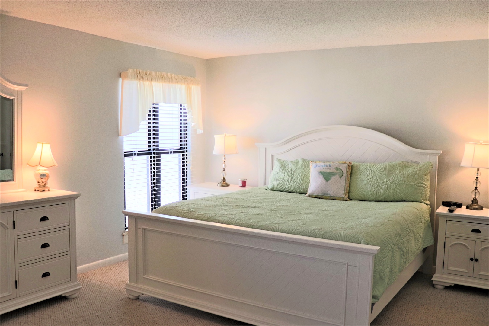 Sink into this peaceful bedroom where soft green linens and warm lighting create your perfect retreat for restful nights.