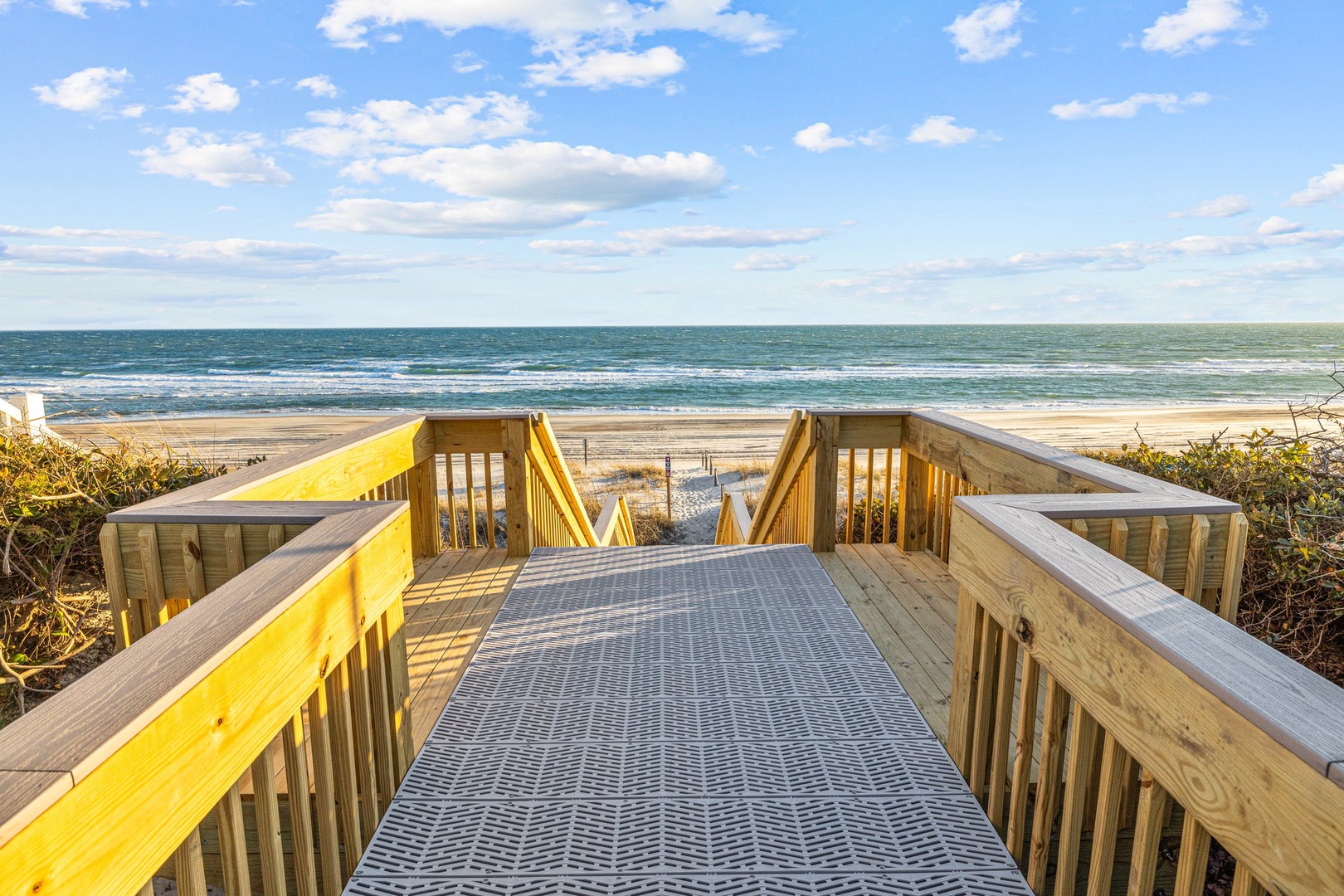 Wooden boardwalk leads directly to pristine sandy beach and ocean waves, offering easy coastal access.