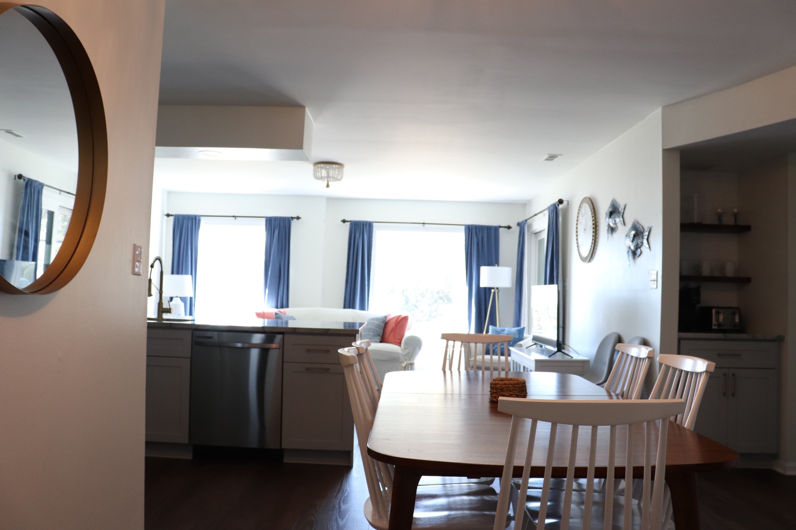 Gather around your spacious dining table for memorable meals, with natural light streaming through blue-framed windows and modern kitchen nearby.