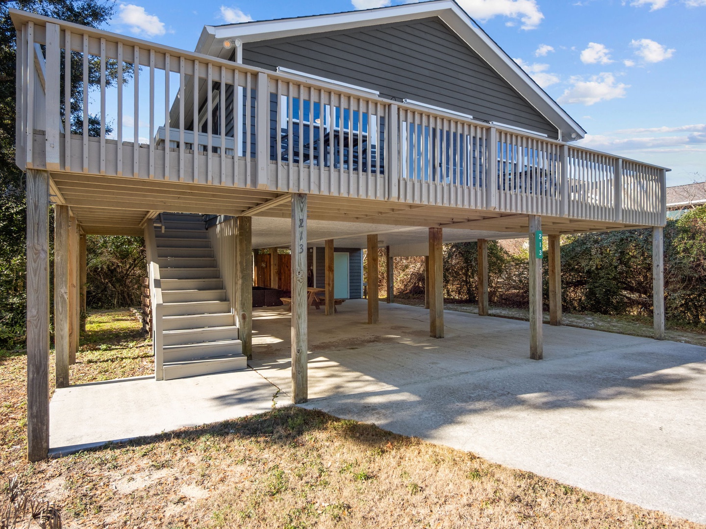 Elevated beach house with wraparound deck, covered parking below, and stairs leading to your coastal retreat.