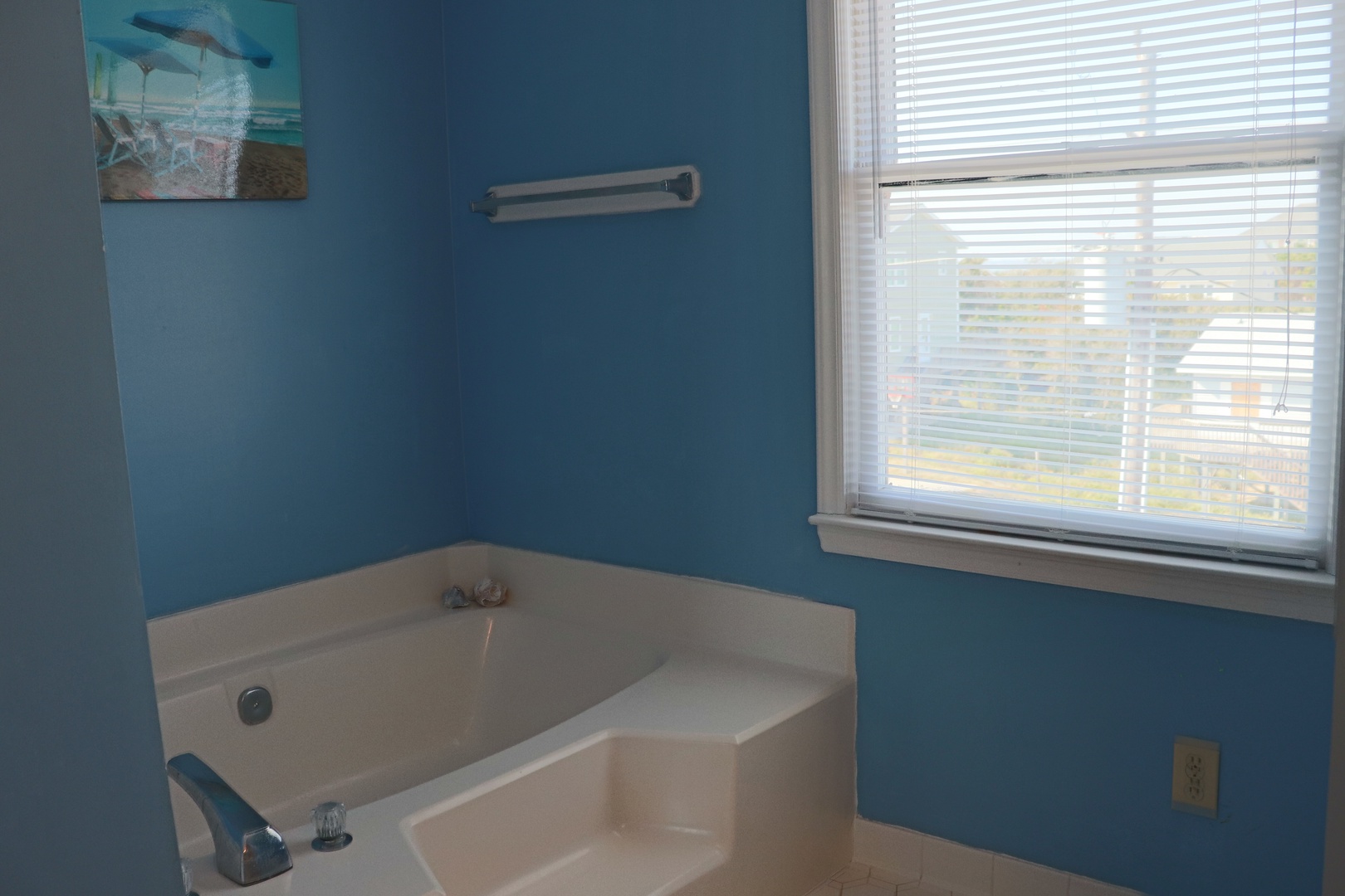 Unwind in your private soaking tub, where ocean-blue walls create a serene spa atmosphere. Natural light streams through blinds for peaceful bathing.
