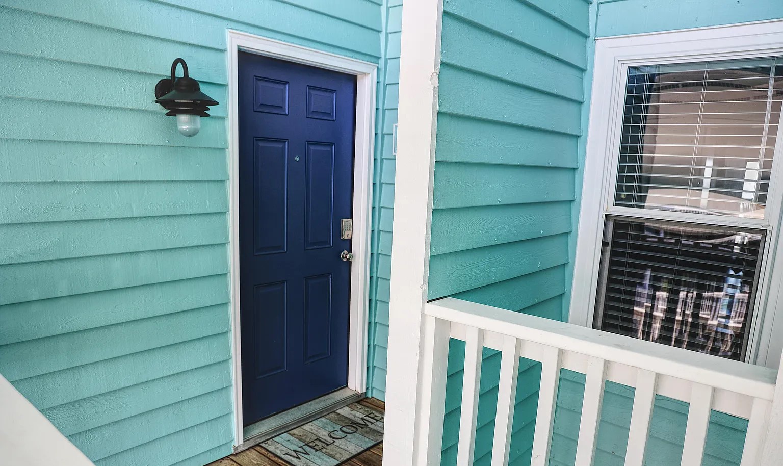 Charming turquoise facade welcomes guests with a classic navy door and welcoming porch light at this coastal-style property.