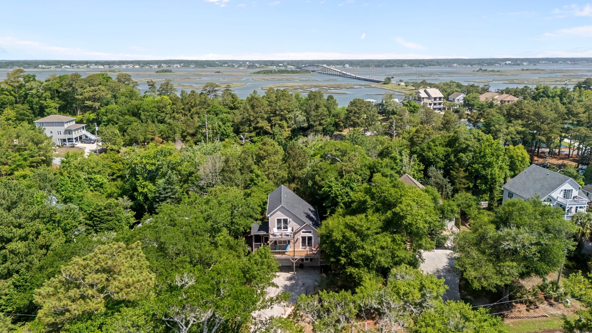 Aerial view of a charming coastal property nestled among lush trees with waterfront access and bridge views in the distance.