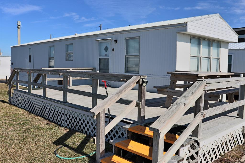 Charming beachside mobile home with spacious deck and wooden stairs, perfect for coastal getaways under bright blue skies.