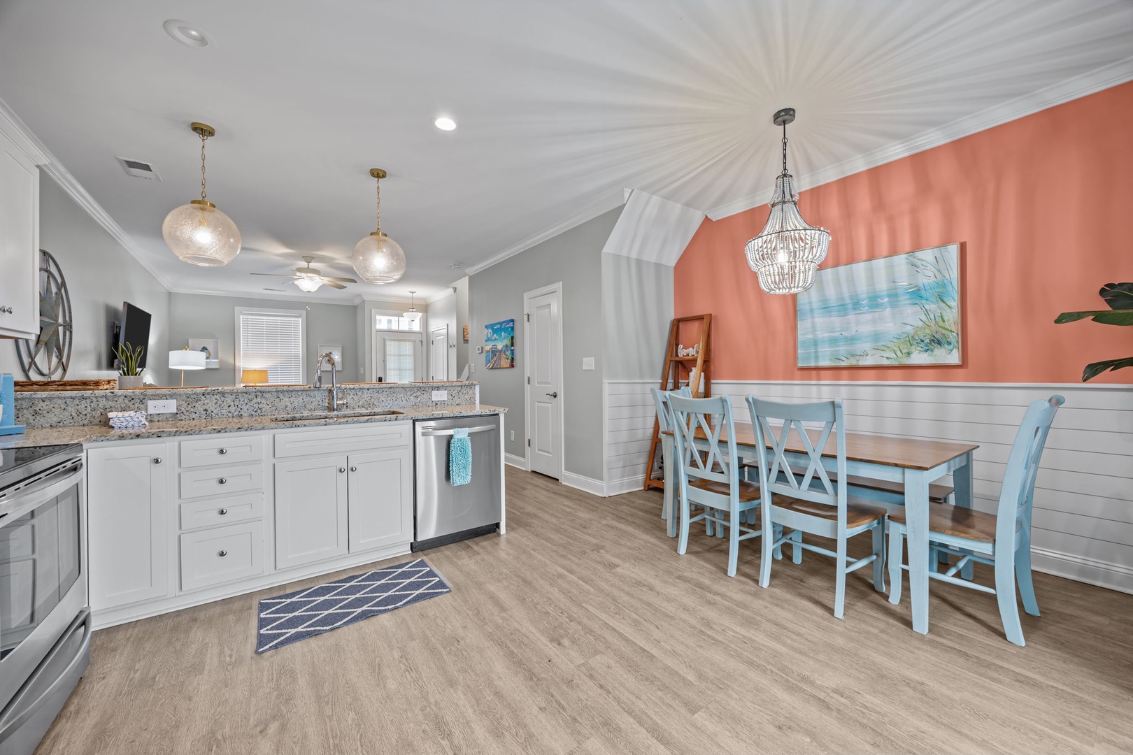 Your bright, coastal-themed kitchen flows seamlessly into the dining area, where warm coral walls and beachy blue chairs create the perfect spot for shared meals.