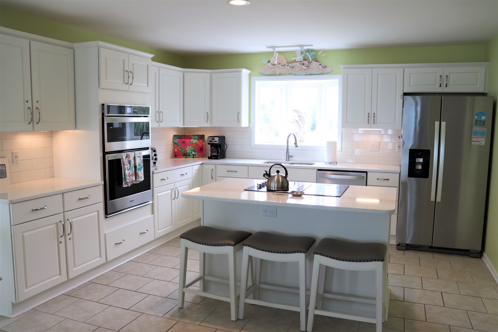 Your spacious kitchen awaits with bright white cabinets, modern appliances, and cheerful green accents creating the perfect space for memorable meals.