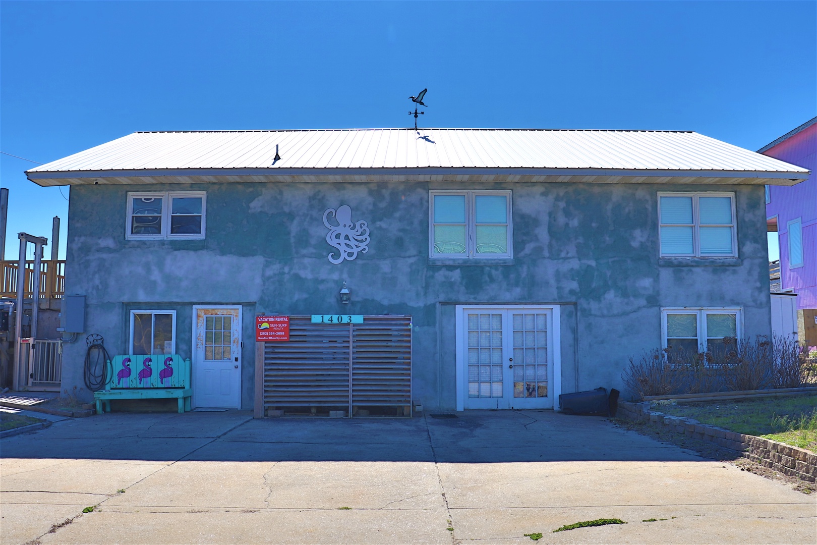 Charming blue coastal building with nautical octopus artwork welcomes guests to their beachside retreat.