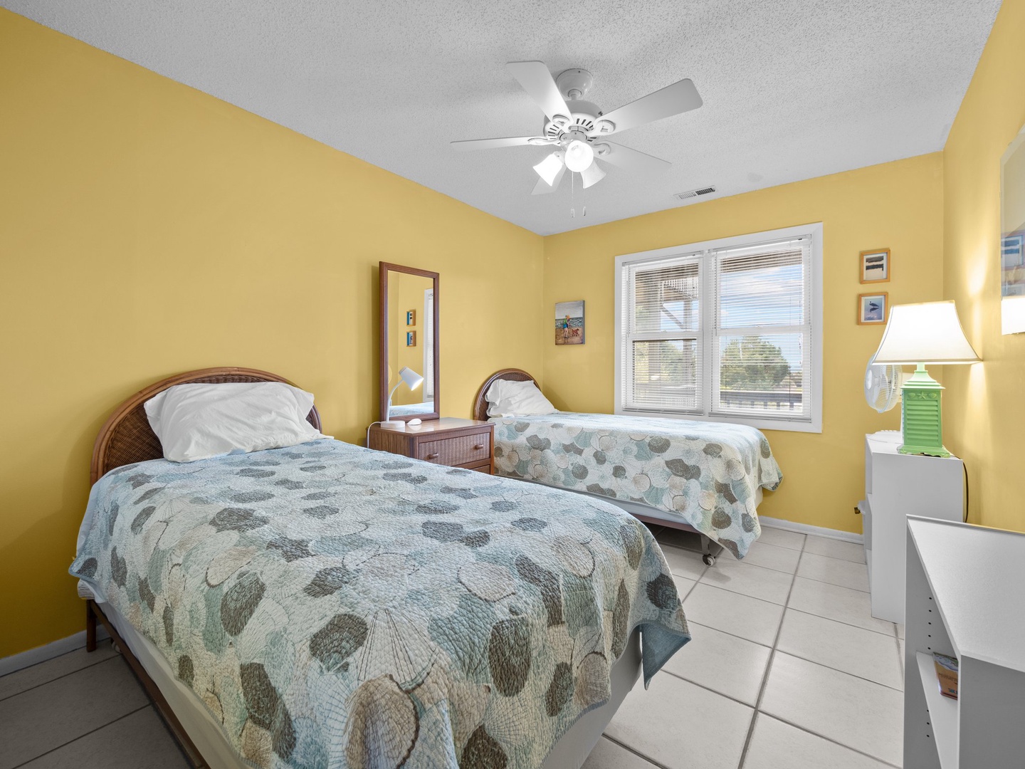 Rest peacefully in this sunny bedroom with twin beds, ceiling fan, and cheerful yellow walls creating your perfect home-away-from-home retreat.