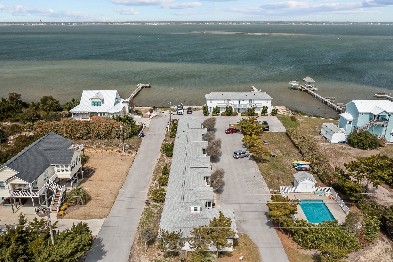 Aerial view of waterfront vacation rentals with private piers extending into calm bay waters, offering direct beach access.