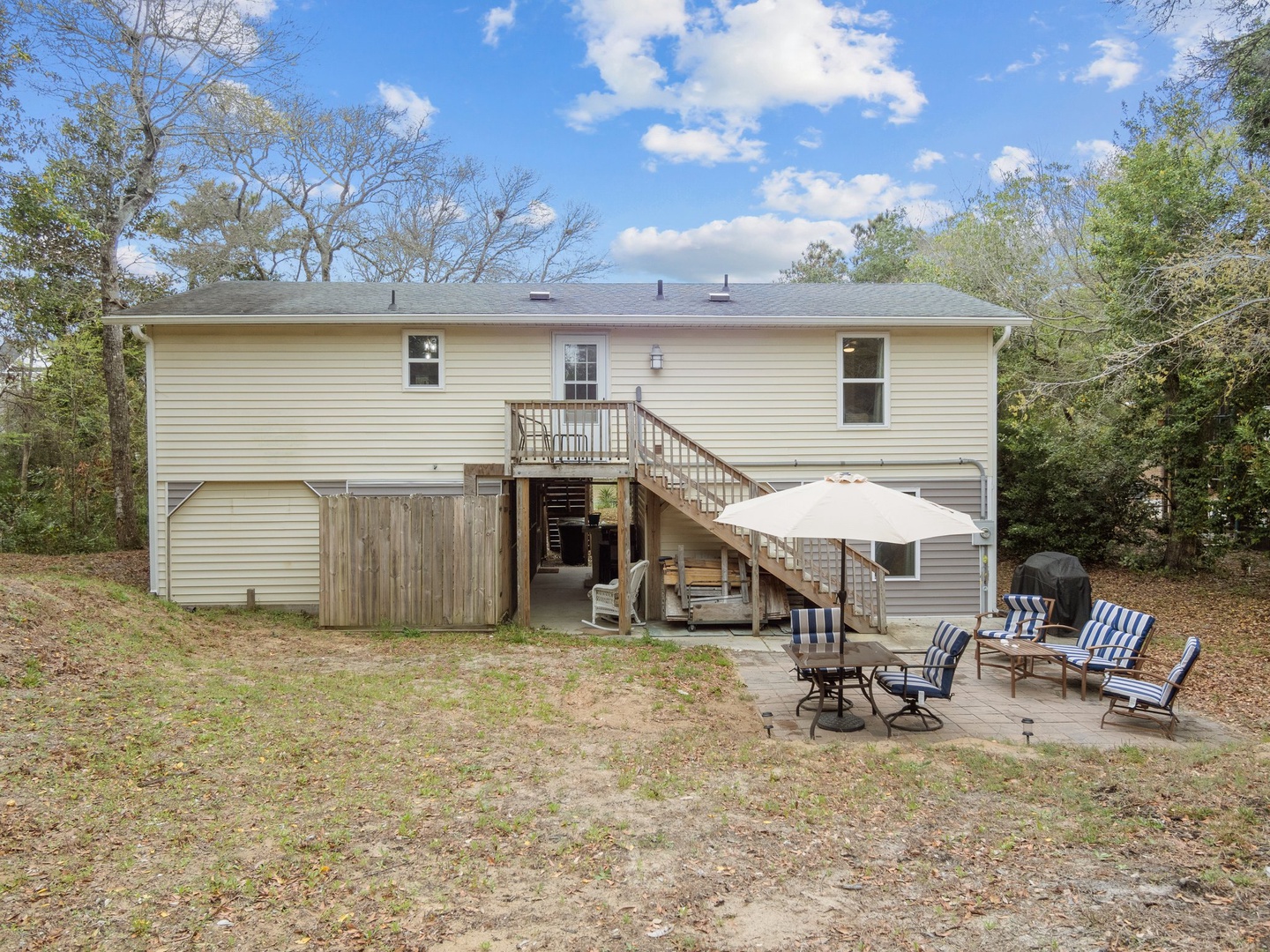 A peaceful two-story vacation home nestled among mature trees, featuring a private backyard patio with comfortable seating and umbrella shade for outdoor relaxation.