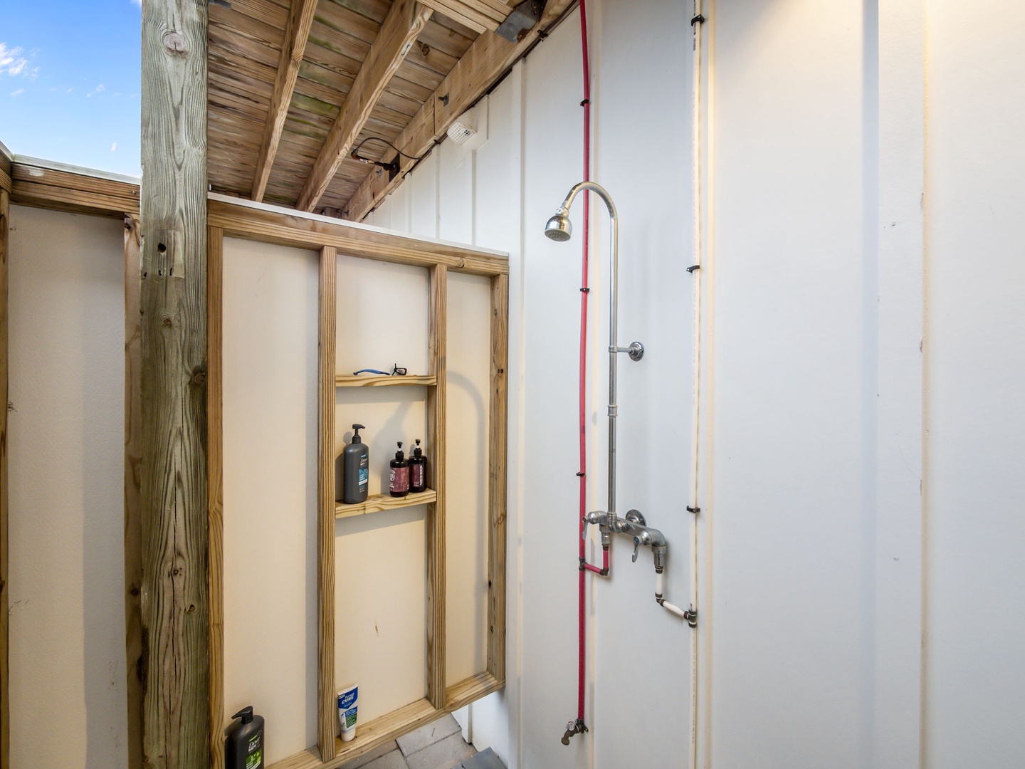 Step into your private outdoor shower with built-in storage for toiletries—open-air bathing under beautiful wooden beams.