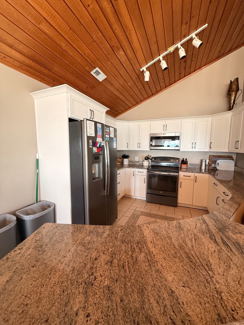 Spacious kitchen with granite countertops, modern appliances, and warm wood-paneled ceilings invites you to prepare delicious meals during your stay.