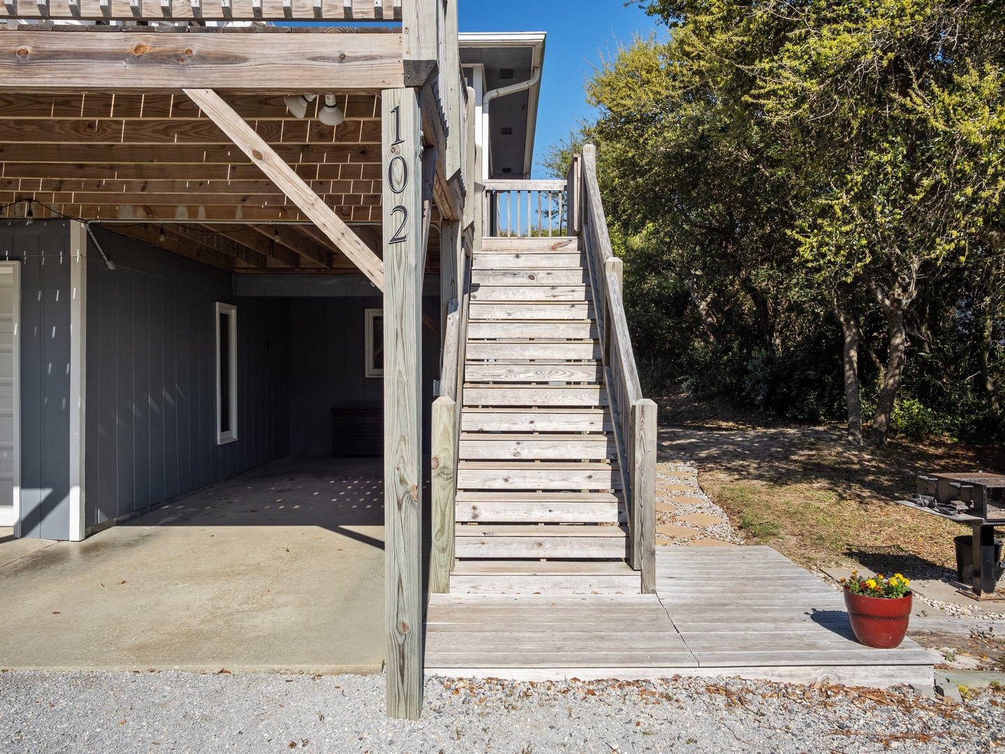 Beach house entrance with wooden stairs leading to your elevated coastal retreat, featuring covered parking and natural landscaping.