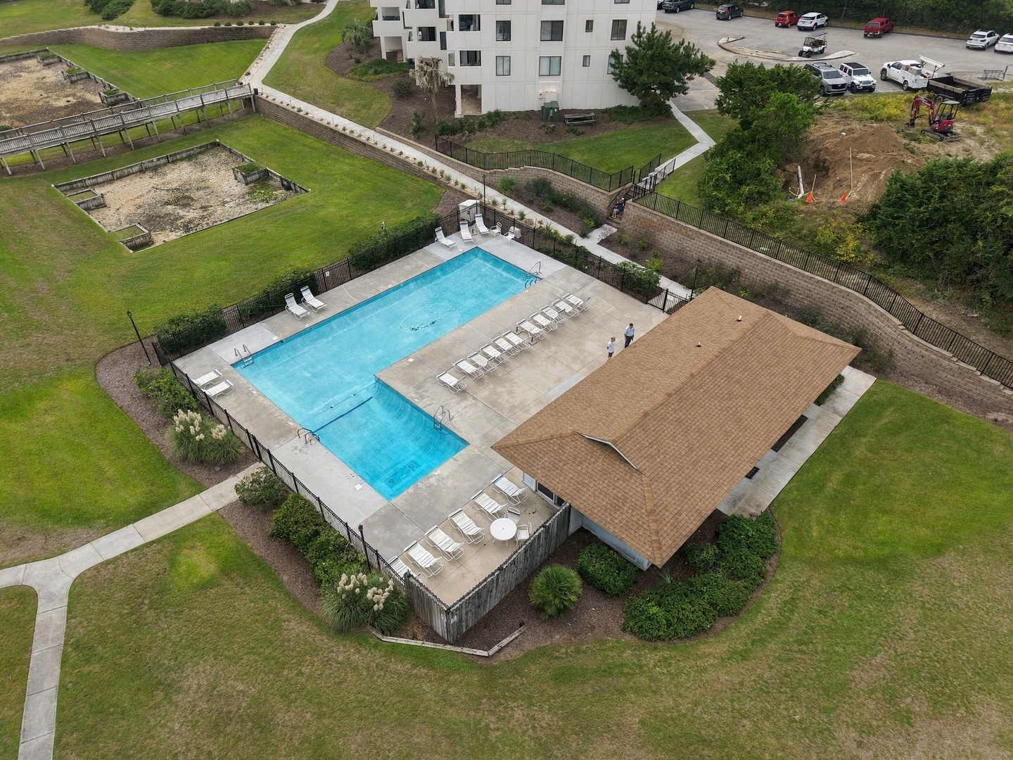 Aerial view showcasing the property's L-shaped swimming pool and covered pavilion, surrounded by landscaped grounds and pathways leading to the main building.