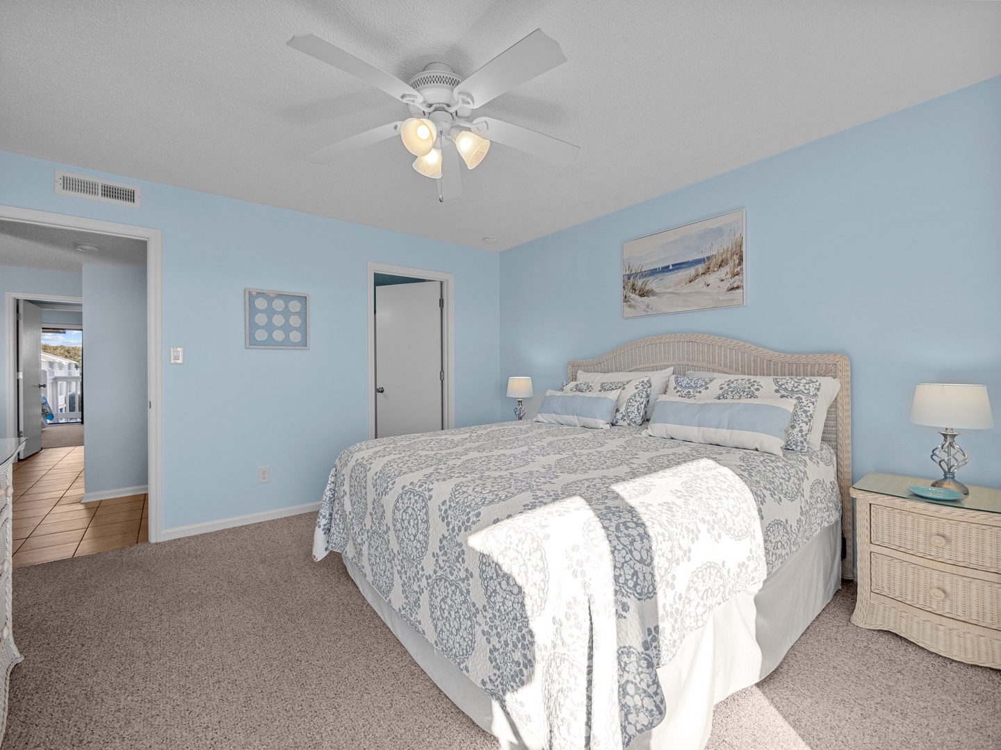 Your serene bedroom features soft blue walls, a comfortable bed with coastal decor, and a ceiling fan for ultimate relaxation.