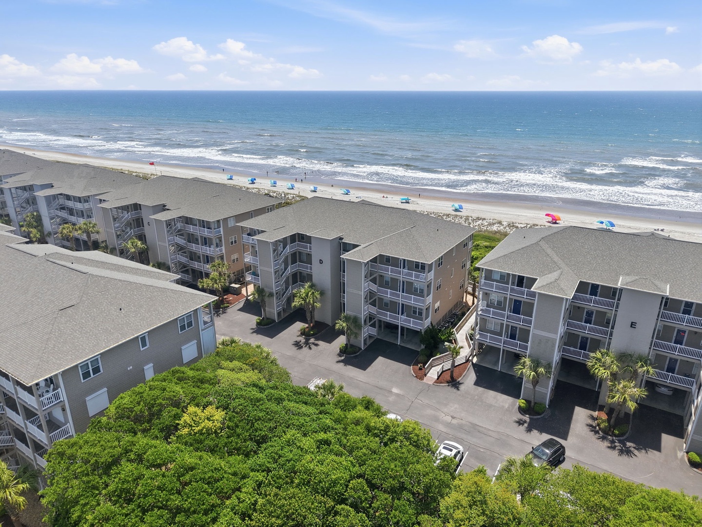 Beachfront property complex with direct ocean access, lush tropical landscaping, and convenient parking facilities along a wide sandy shore.