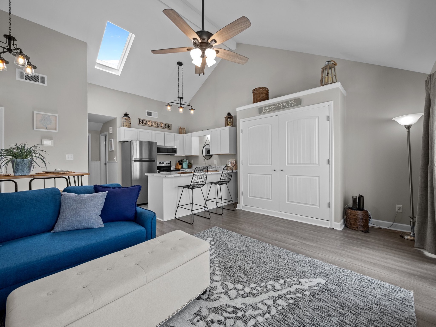 Relax in your bright, airy living space with vaulted ceilings, skylight, and cozy blue sofa opening to a fully equipped kitchen.