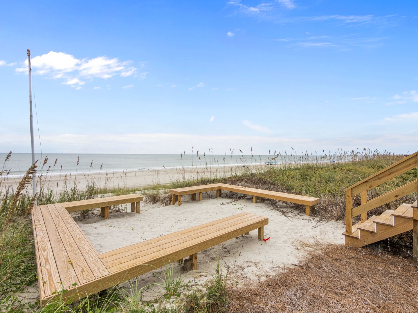 Wooden deck seating area overlooking pristine sandy beach and ocean waters with convenient beach access.