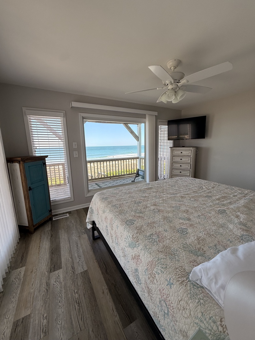 Unwind in your serene bedroom featuring a plush bed with elegant linens, coastal-inspired textures, and natural light streaming through privacy-filtered windows. A ceiling fan keeps you comfortable year-round.