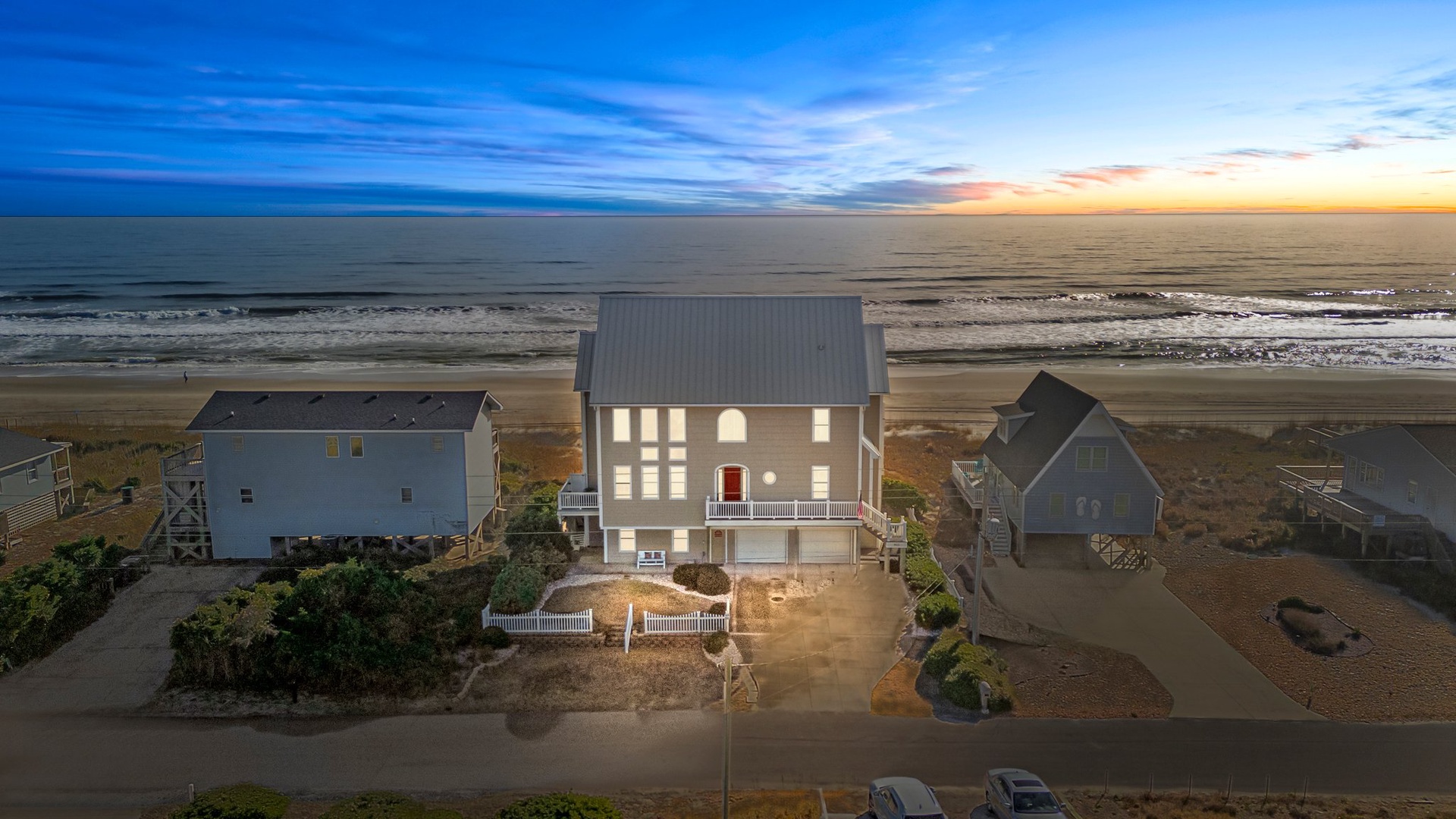 Stunning beachfront property positioned directly on the sandy shore with panoramic ocean views and neighboring coastal homes at sunset.
