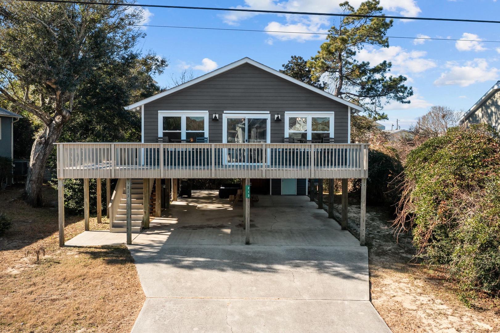 Charming elevated beach house with spacious deck and covered parking area nestled among mature trees.