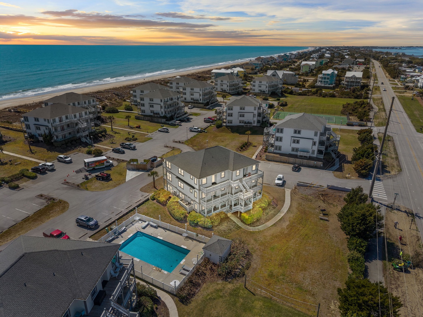 Stunning aerial view of beachfront vacation rental community with ocean access, swimming pool, and coastal charm at sunset.