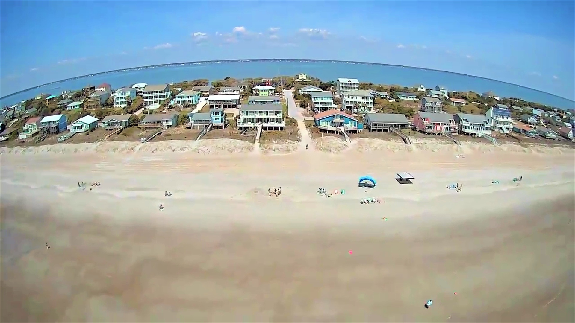Stunning aerial view of the beachfront community with colorful homes dotting the pristine coastline and crystal-clear waters stretching to the horizon.