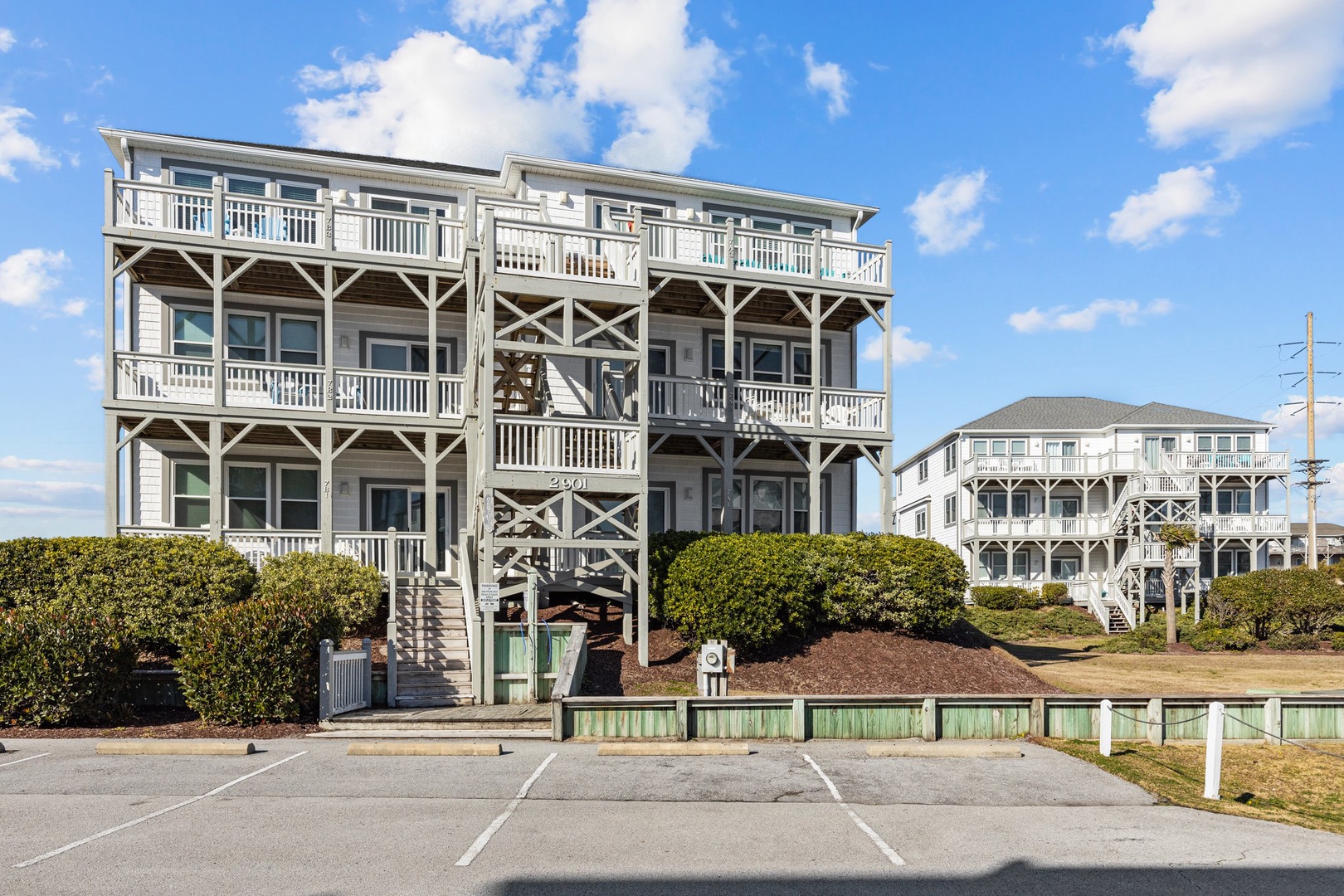 Multi-story beachfront property with white railings and elevated design on stilts, featuring dedicated parking spaces.
