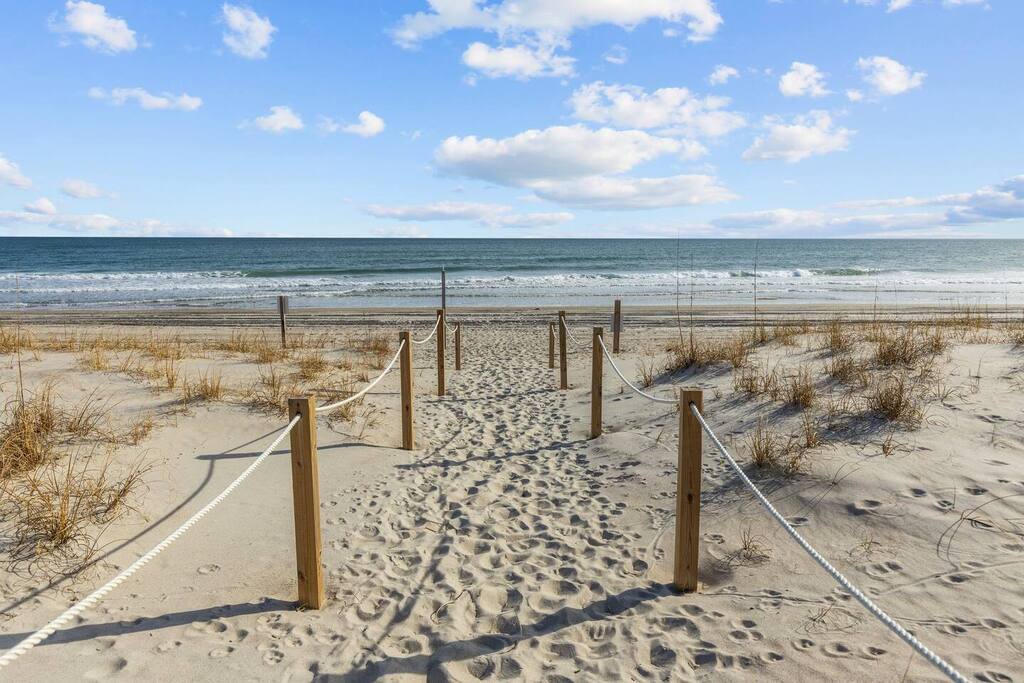 Sandy beach access with wooden boardwalk leading to pristine coastline under blue skies.