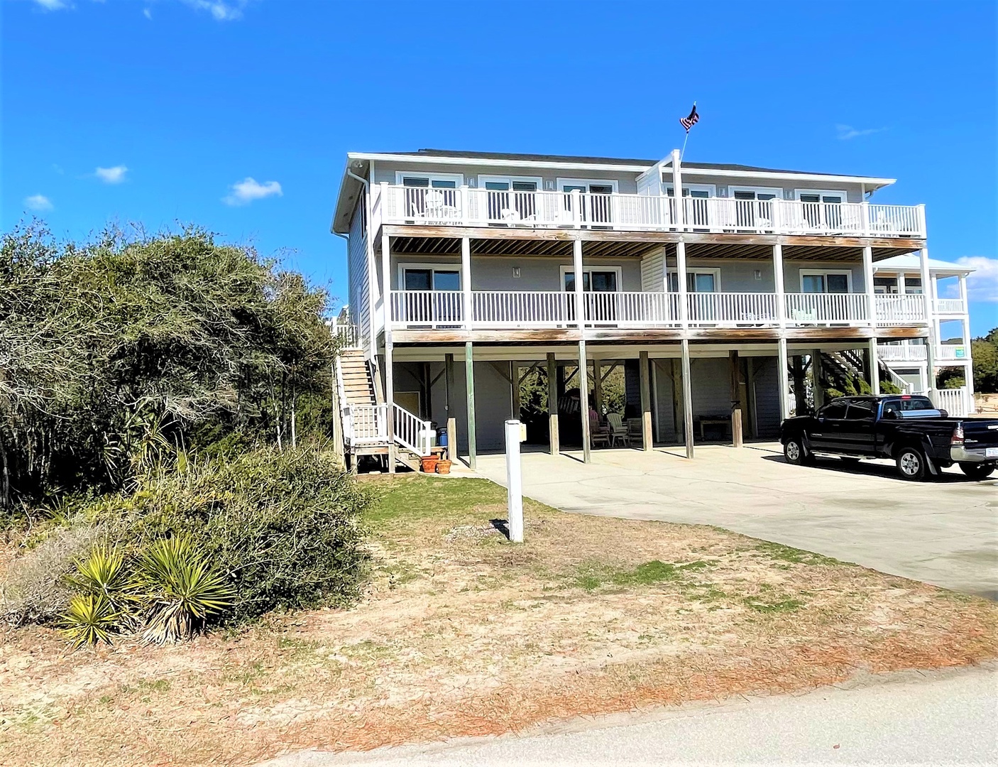 Multi-level beach house with wraparound balconies and covered parking, perfectly positioned near coastal vegetation.