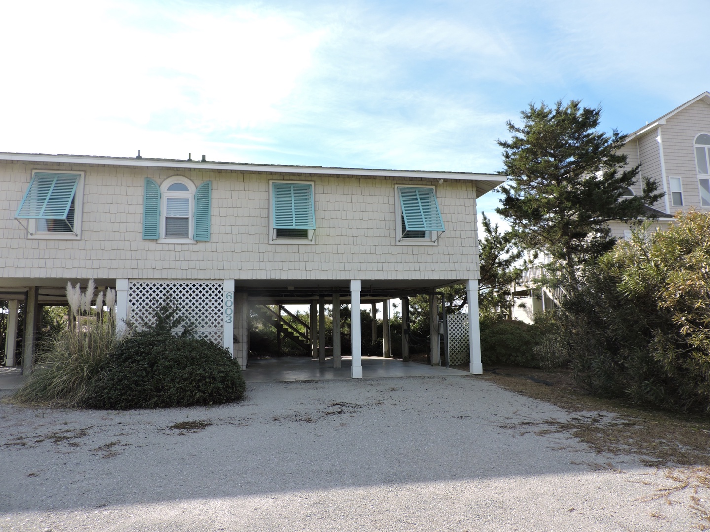 Charming elevated beach house with turquoise shutters and covered parking in a peaceful coastal neighborhood.