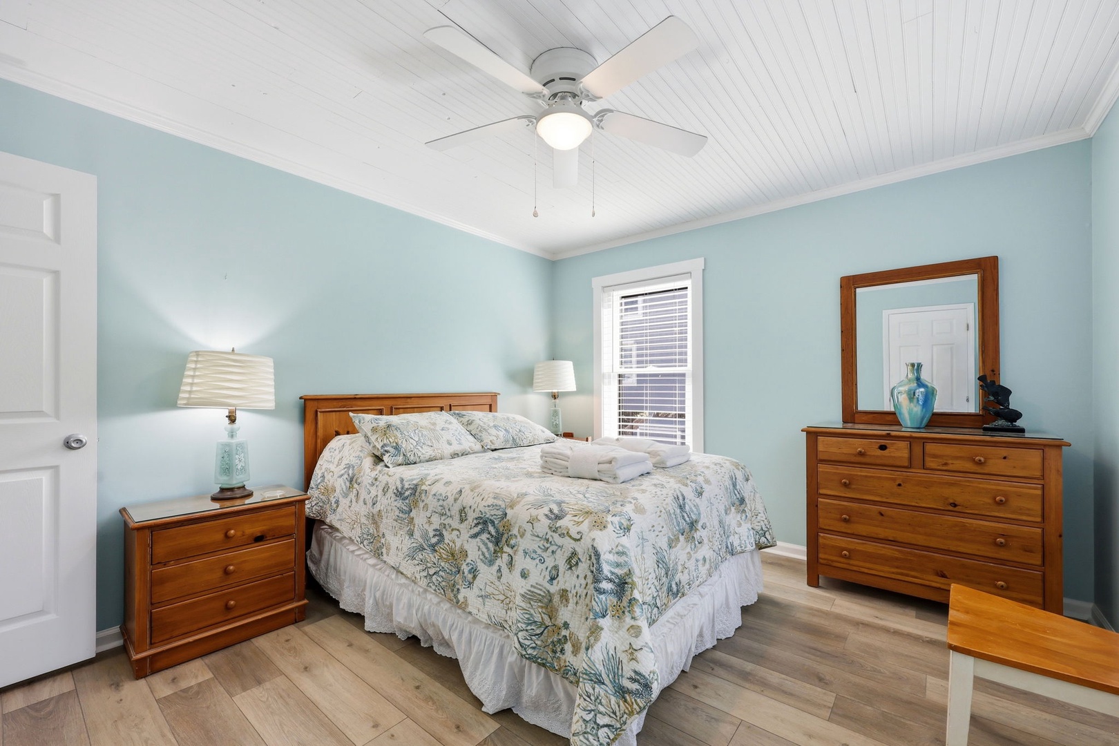 Unwind in your serene coastal bedroom, where soothing aqua walls and crisp white ceilings create a tranquil retreat. The ceiling fan keeps you comfortable while warm wood accents add charm.