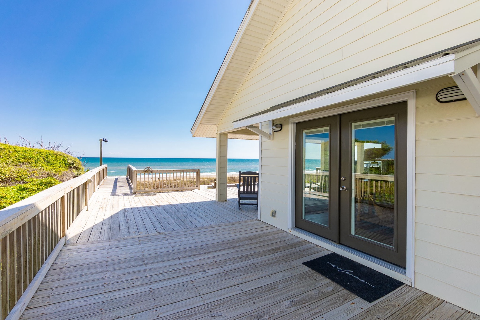 Beachfront property featuring a spacious deck with direct ocean access via wooden boardwalk to pristine sandy shores.