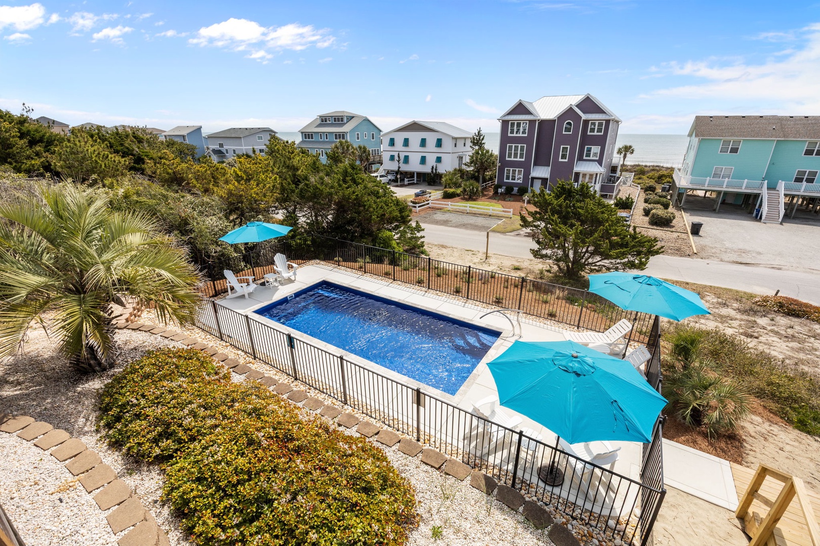 Aerial view of the pool area with blue umbrellas, surrounded by colorful beach houses in a coastal neighborhood setting.